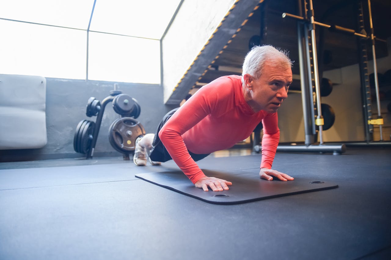 Senior man doing push-ups on a mat in a gym setting, emphasizing fitness.